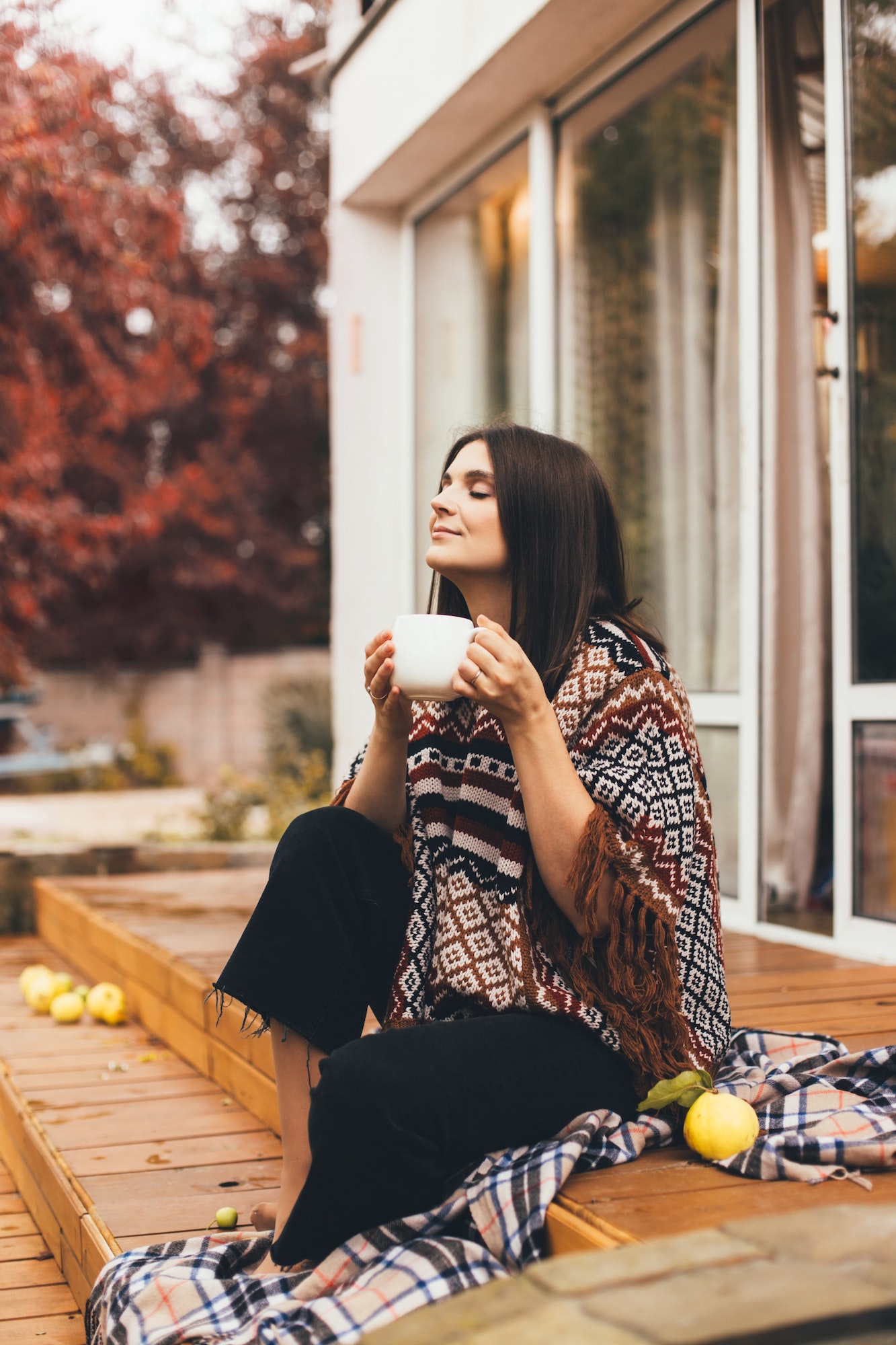 Young woman sitting on wooden porch of a cozy country house and drinking hot tea.